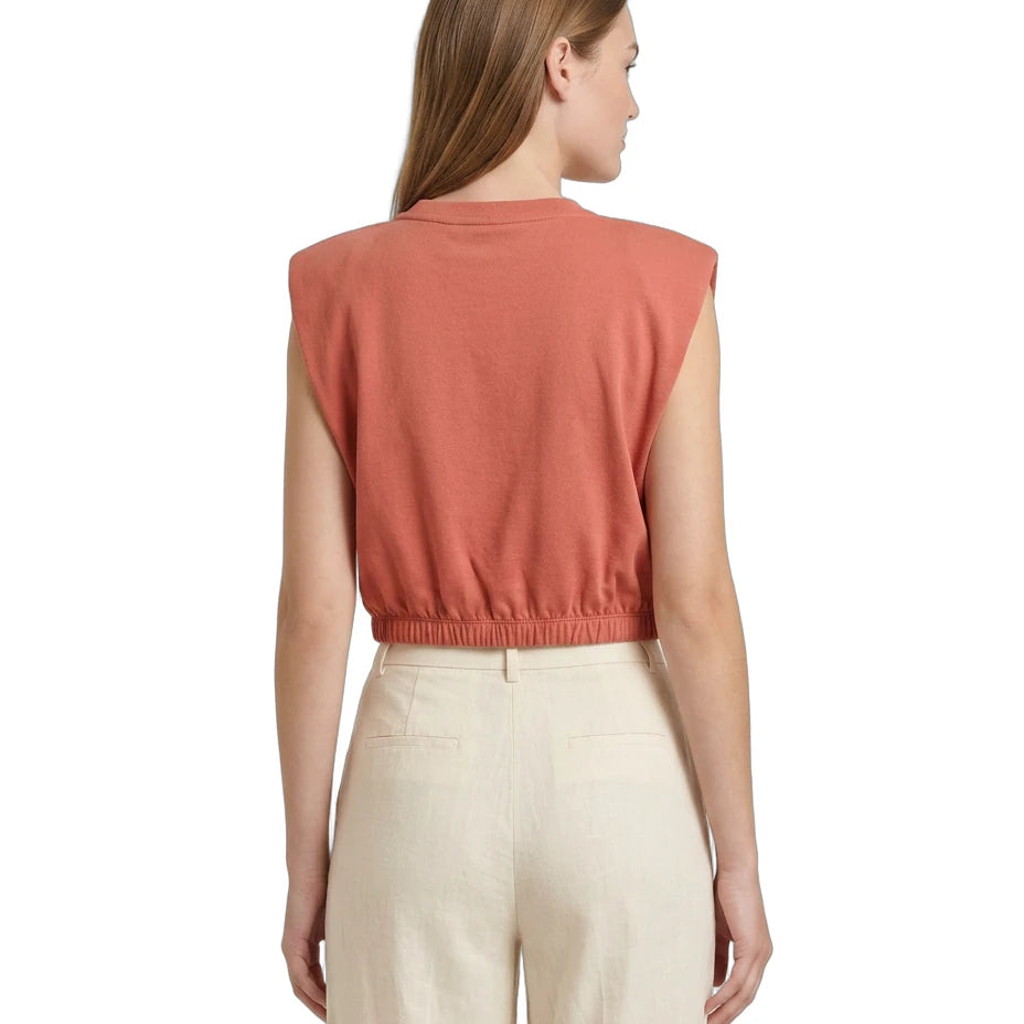 Woman wearing a sleeveless rust-colored top and beige pants on a white background