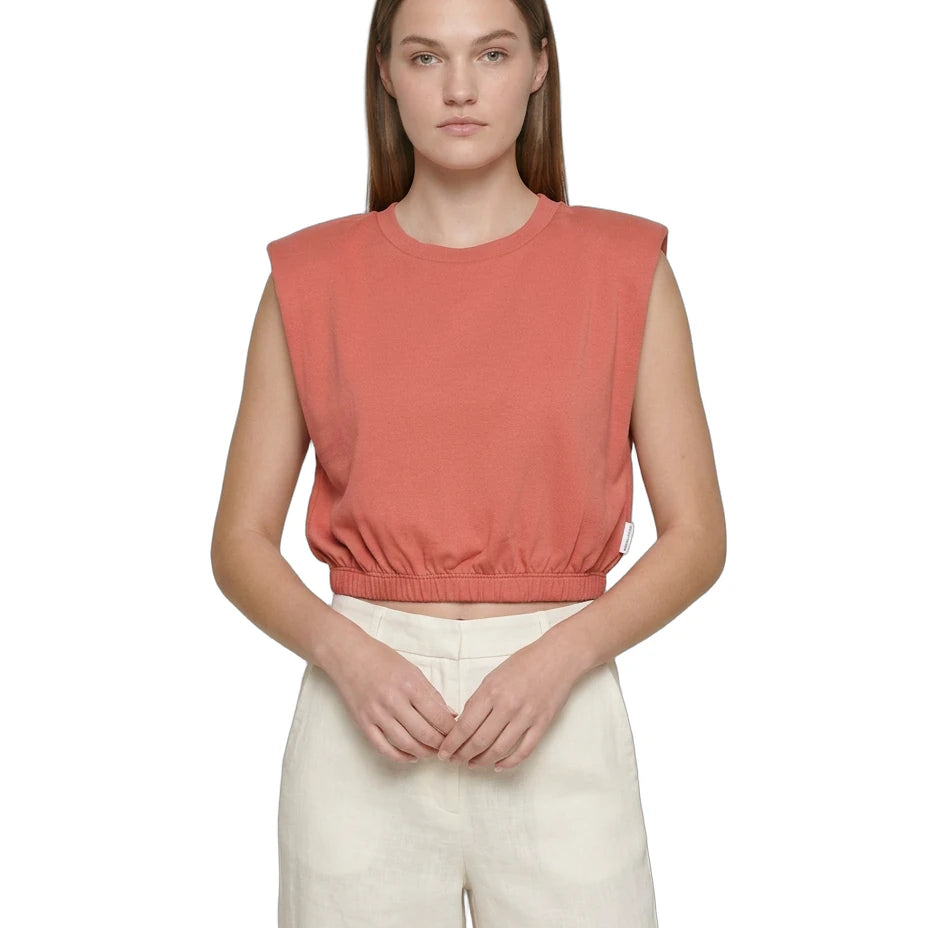 Woman wearing a coral sleeveless top and white pants on a white background