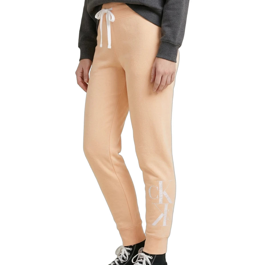 Person wearing beige jogger pants with a logo, black sneakers, and a gray sweatshirt on a white background.