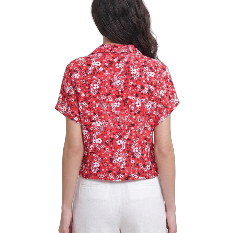 Woman wearing a red floral Calvin Klein blouse with white pants on a white background