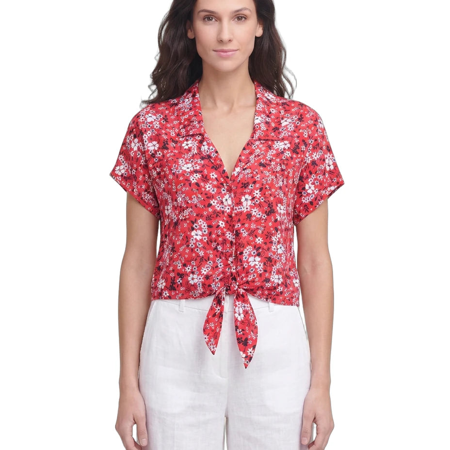 Woman wearing a red floral Calvin Klein blouse and white pants on a white background