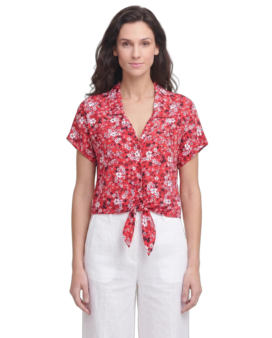 Woman wearing a red floral Calvin Klein blouse and white pants on a white background