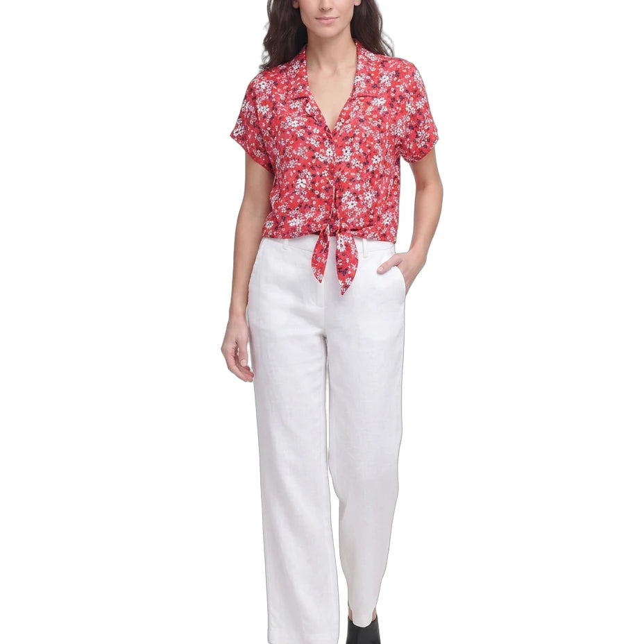 Woman wearing a red floral Calvin Klein blouse and white pants on a white background