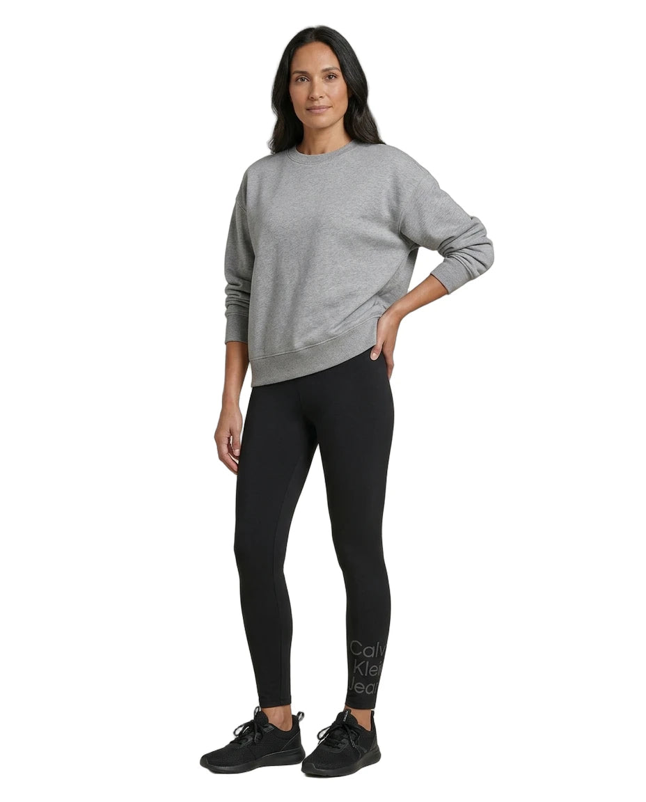 Woman wearing a gray sweater and black Calvin Klein leggings on a white background