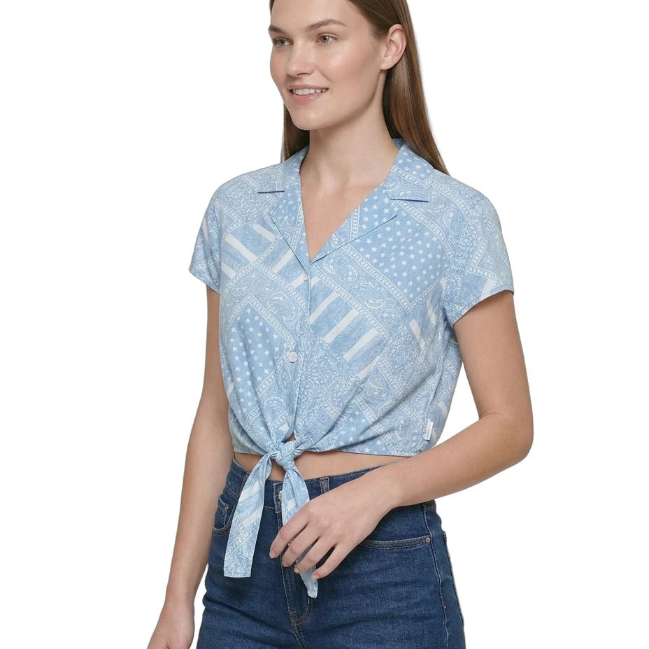 Woman wearing a light blue patterned Calvin Klein shirt and denim shorts on a white background