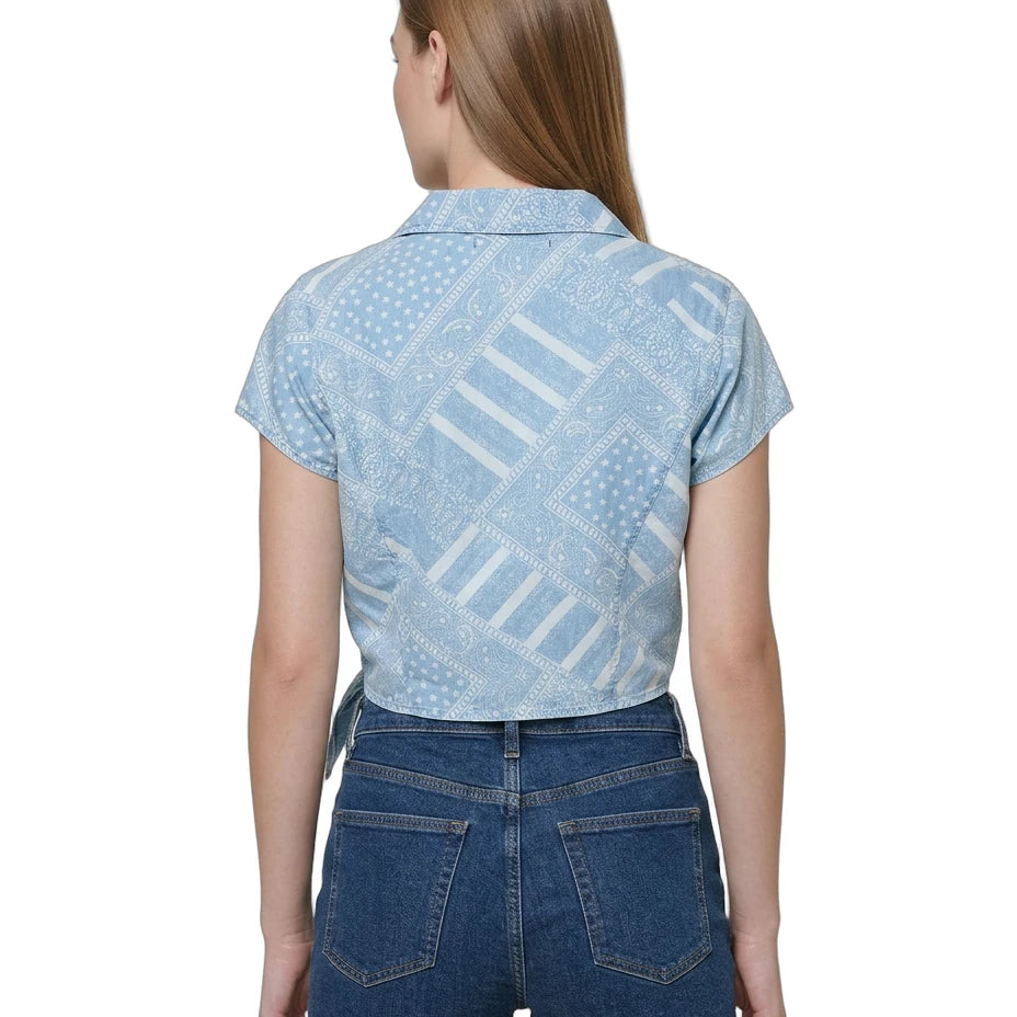 Woman wearing a light blue patterned Calvin Klein shirt and denim shorts on a white background