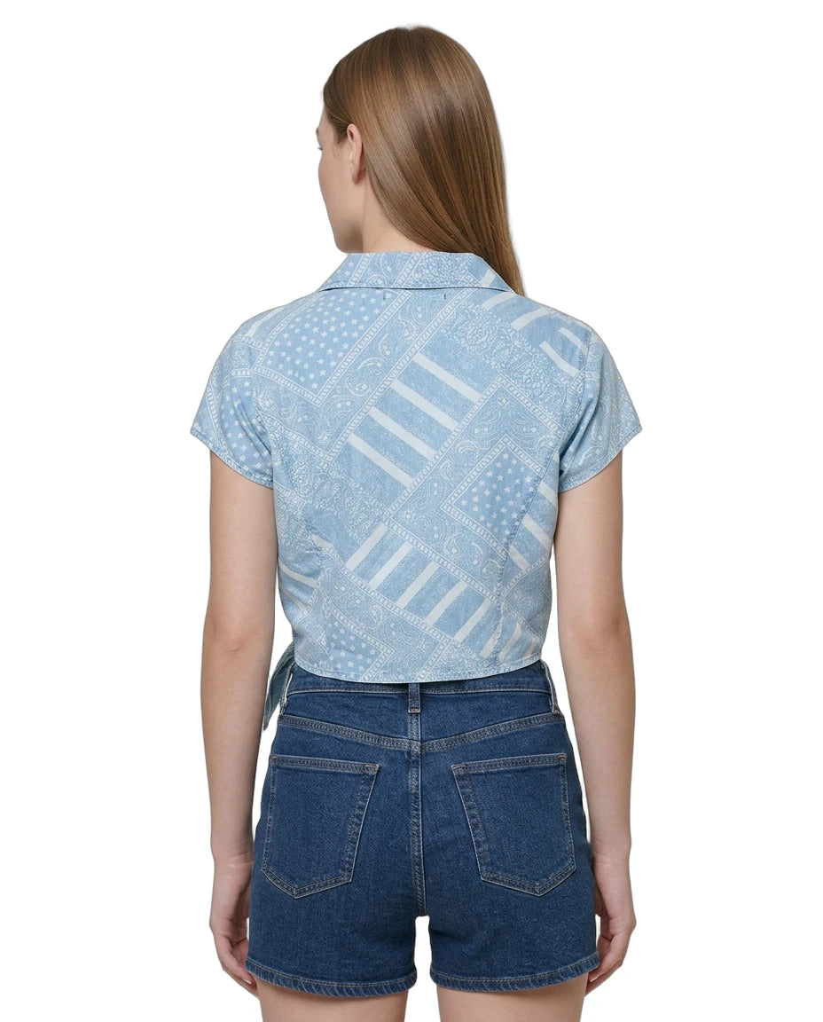 Woman wearing a light blue patterned Calvin Klein shirt and denim shorts on a white background