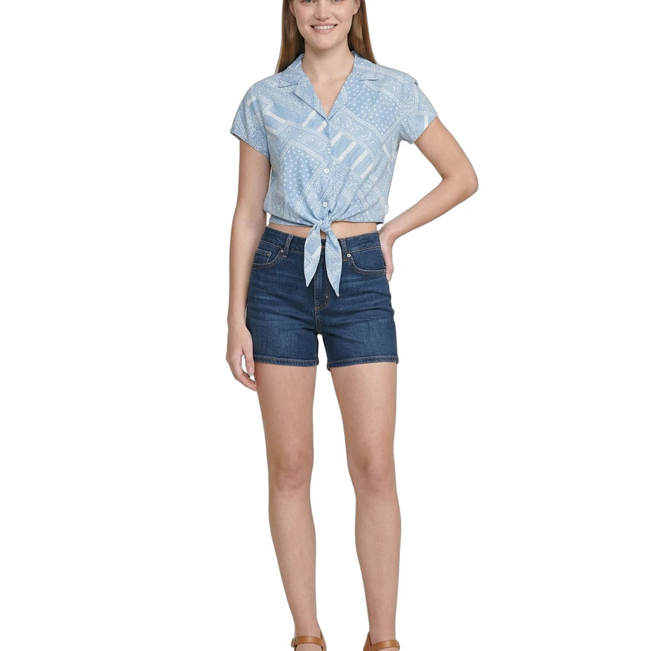 Woman wearing a blue patterned Calvin Klein top and denim shorts on a white background