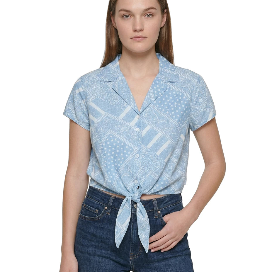 Woman wearing a light blue patterned Calvin Klein shirt and denim shorts on a white background