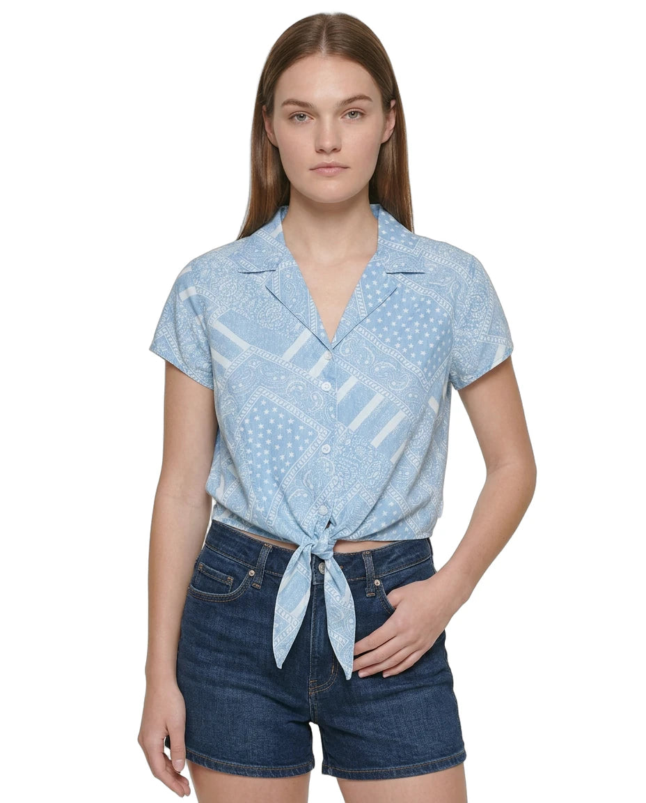 Woman wearing a light blue patterned Calvin Klein shirt and denim shorts on a white background