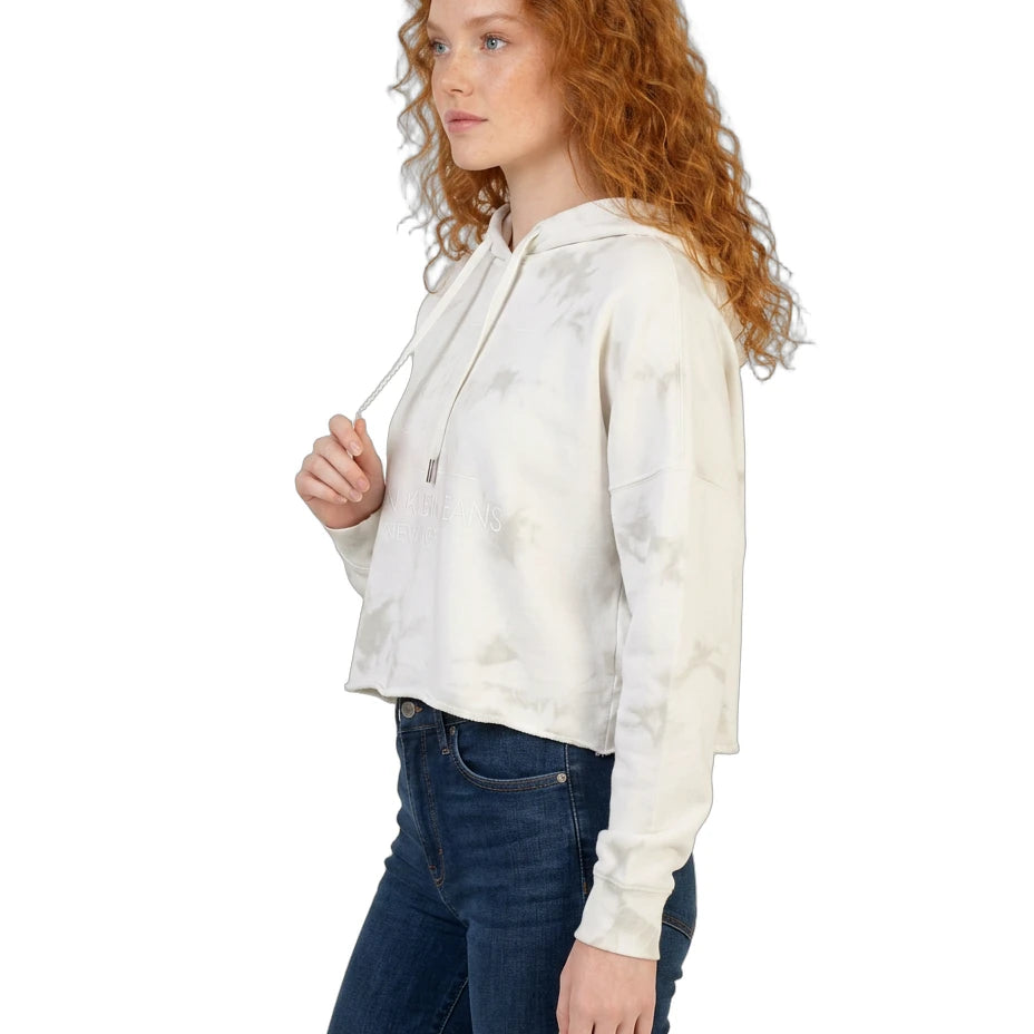 Woman wearing a white tie-dye Calvin Klein hoodie and dark jeans on a white background