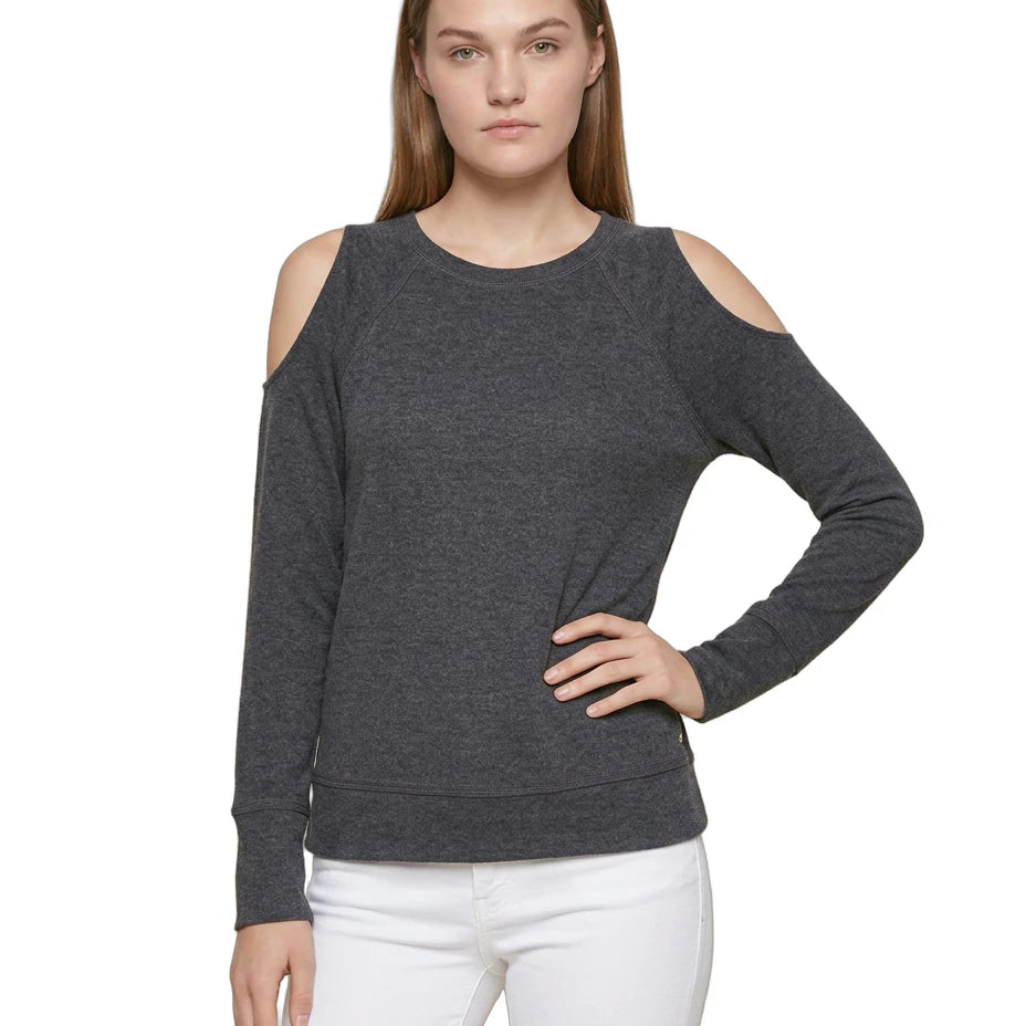 Woman wearing a dark gray cold-shoulder sweater with white pants on a white background