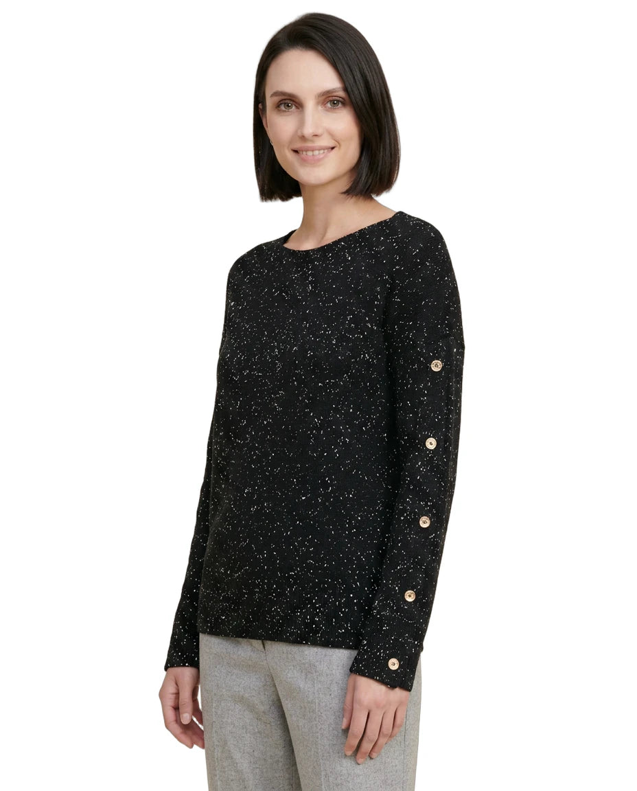 Woman wearing a black speckled sweater with gold buttons on a white background