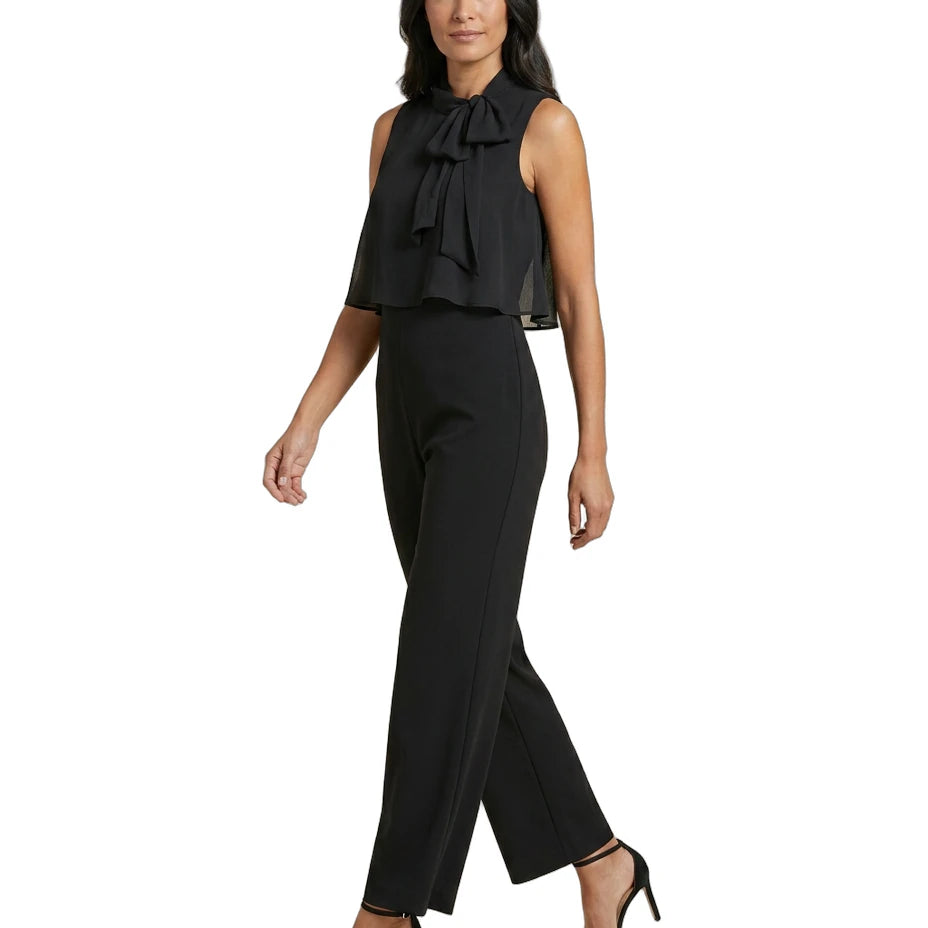 Woman wearing a black sleeveless top with a bow and black pants on a white background