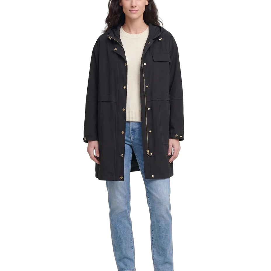 Woman wearing a black Calvin Klein coat, beige sweater, and blue jeans on a white background
