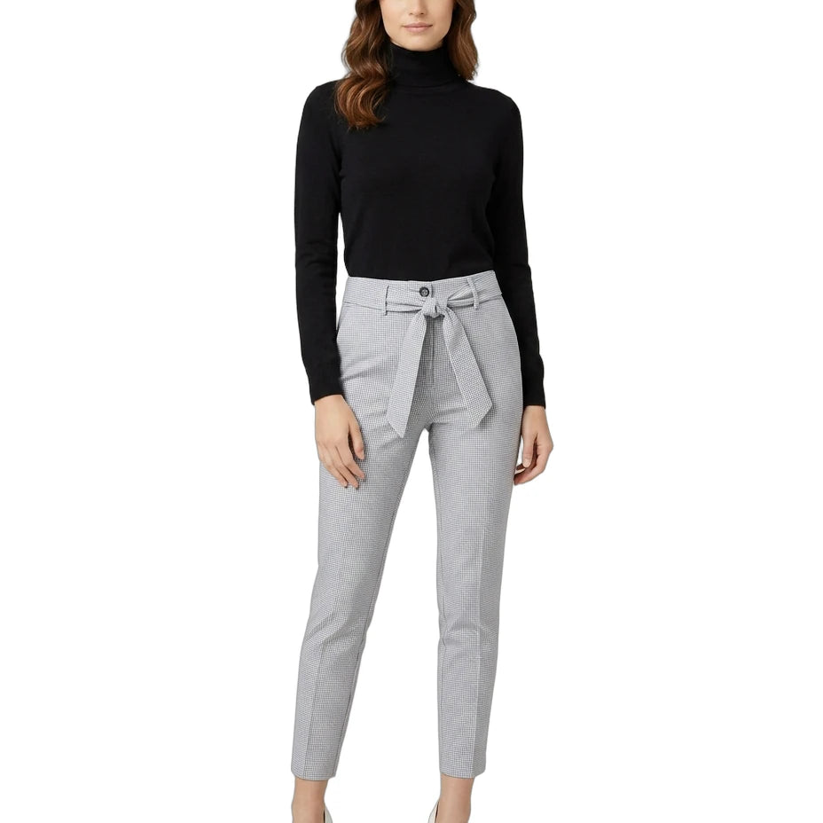 Woman wearing a black turtleneck and gray Calin Klein pants with a belt on a white background
