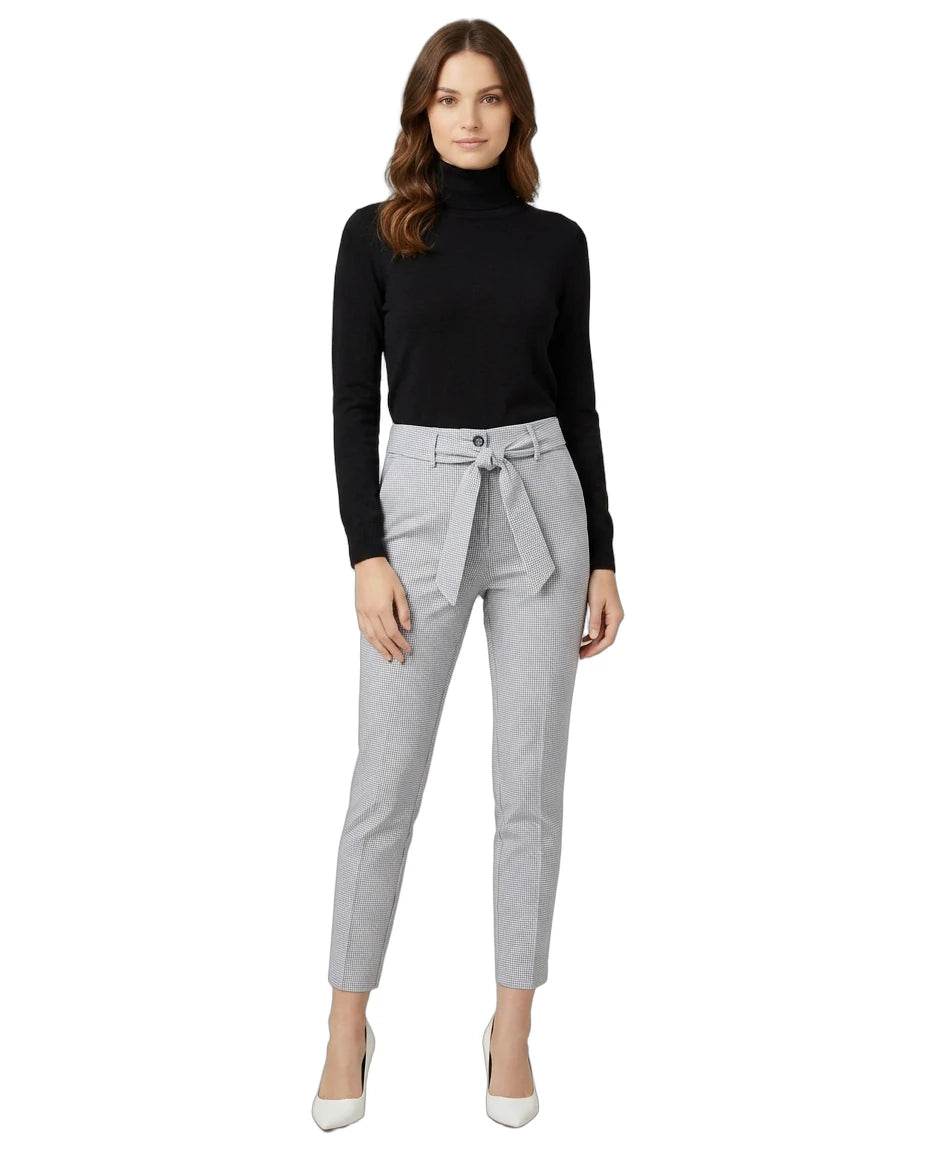 Woman wearing a black turtleneck and gray Calin Klein pants with a belt on a white background