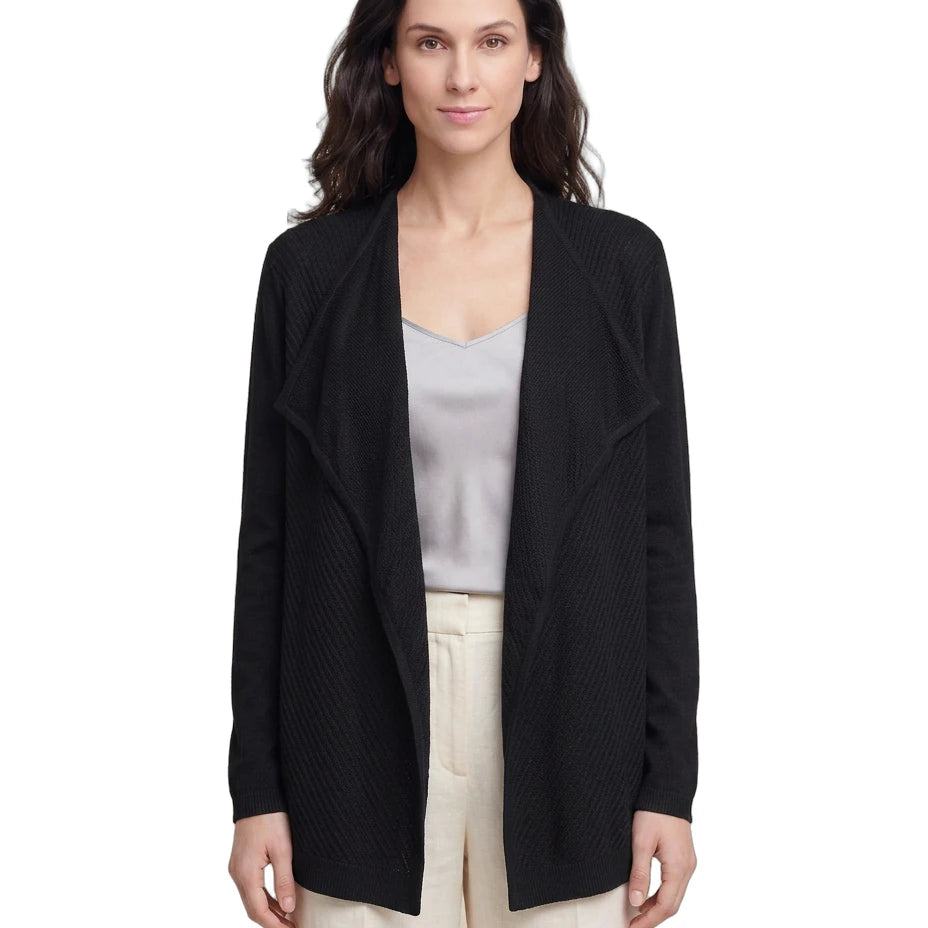 Woman wearing a black Calvin Klein cardigan over a light gray top and beige pants on a white background