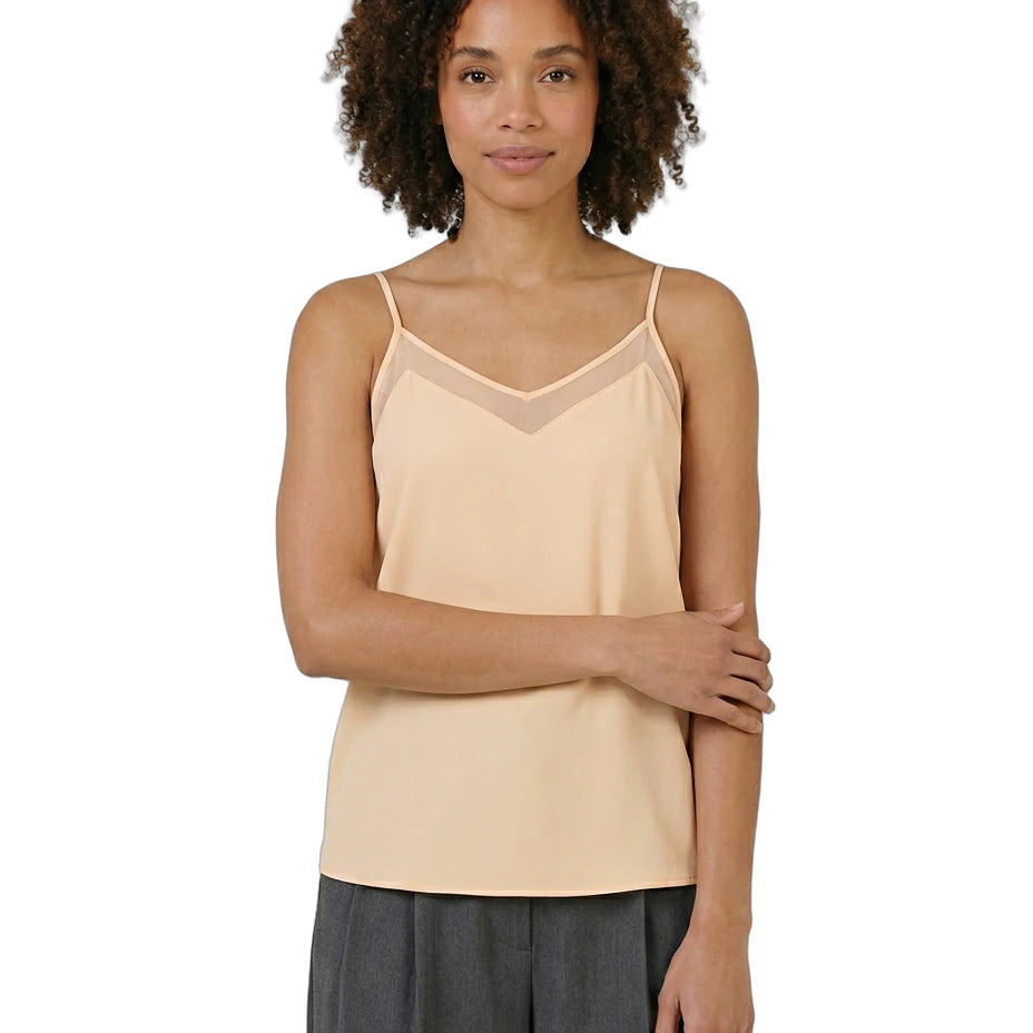 Woman wearing a beige camisole and gray pants on a white background