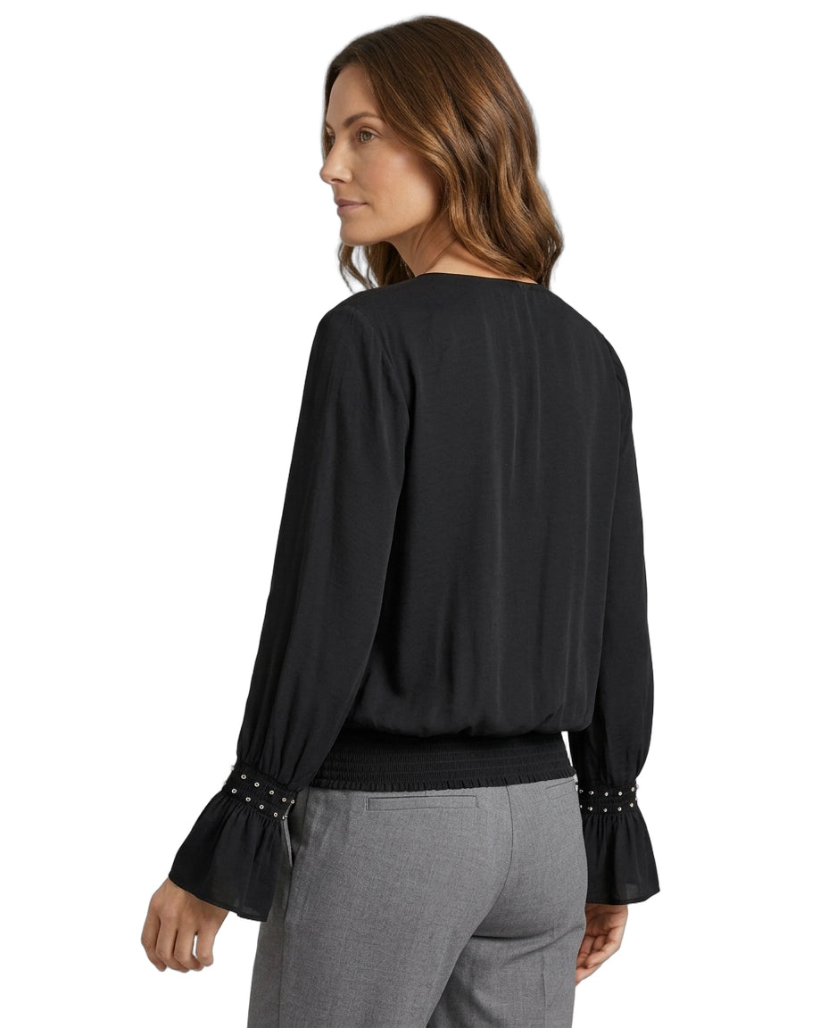 Woman wearing a black blouse with long sleeves and gray pants on a white background