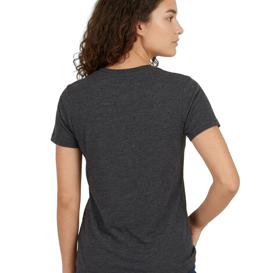 A woman with curly brown hair is shown from the back wearing a dark heather gray short-sleeve t-shirt and blue jeans against a plain white background.