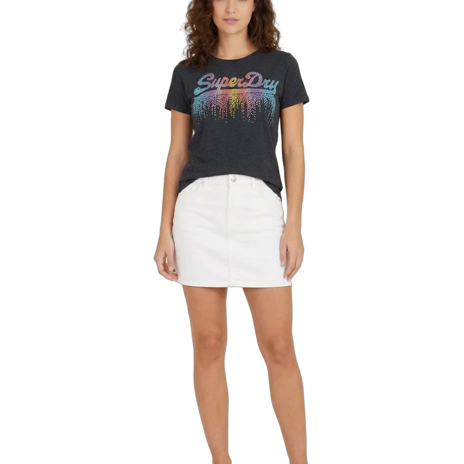 A woman modeling a dark charcoal gray Superdry t-shirt with a colorful gradient 'SuperDry' logo and white denim mini skirt, paired with black sandals, against a plain white background.
