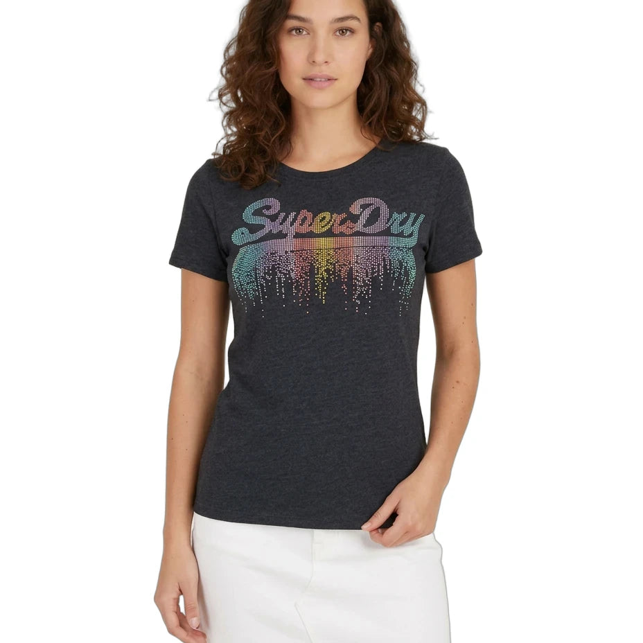 A woman modeling a dark charcoal heather t-shirt with a colorful 'SuperDry' graphic across the chest, paired with a white mini skirt, against a plain white background.