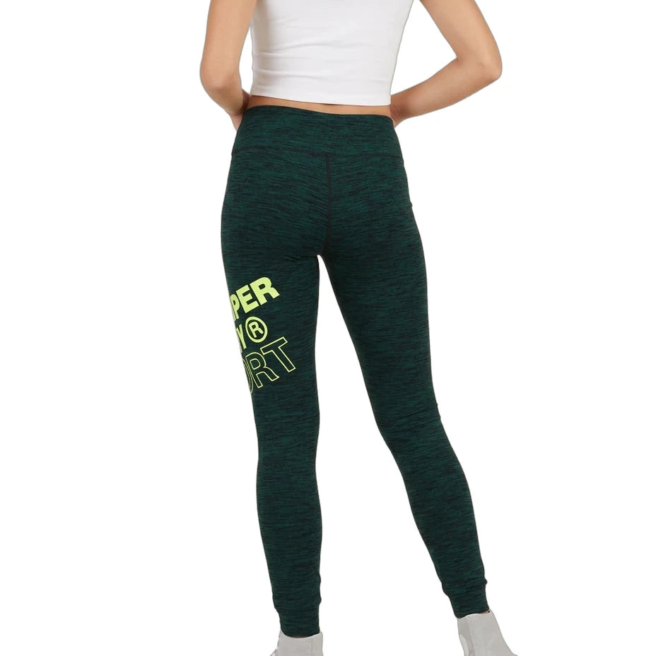 A model from the back wearing dark green heathered leggings with a bright yellow-green graphic text print on the left leg, paired with a white crop top and white sneakers, against a plain white background.