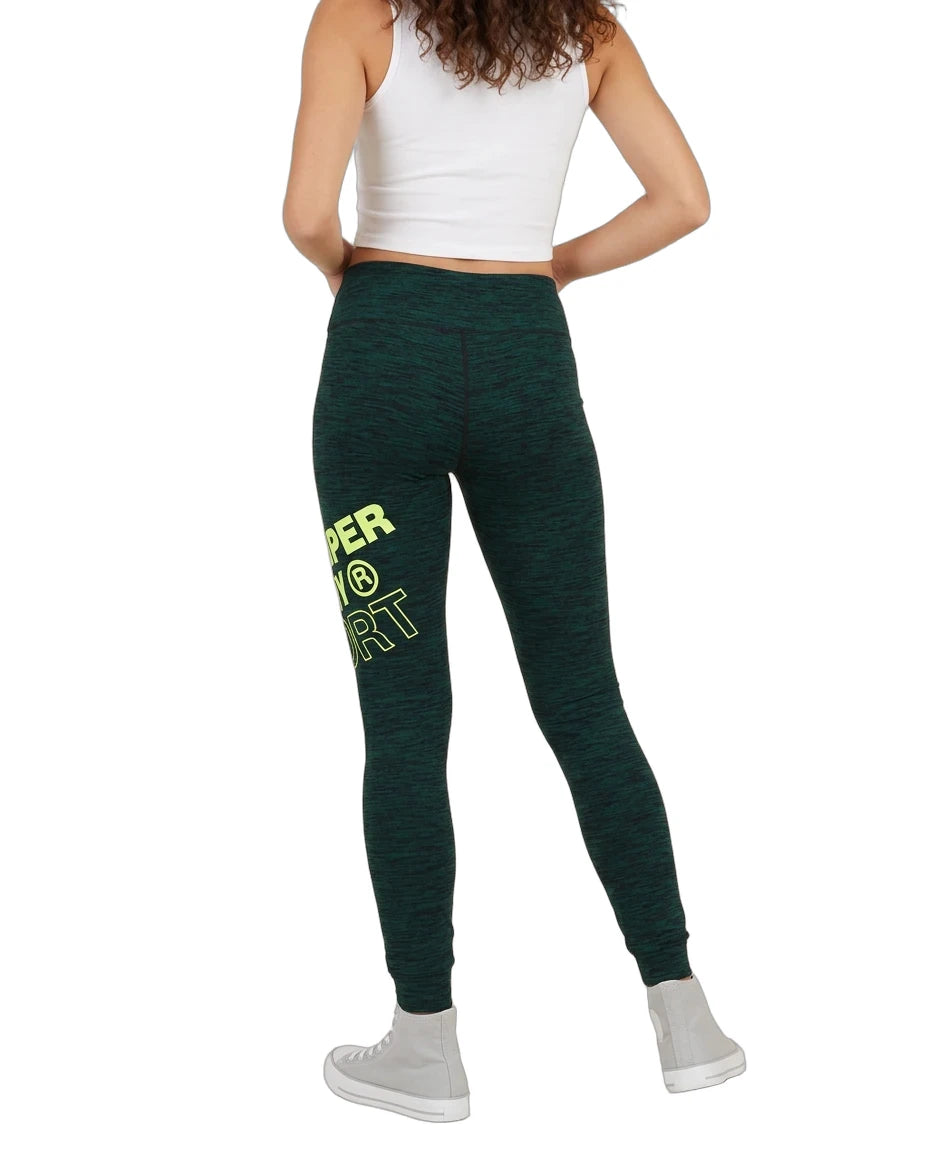 A model from the back wearing dark green heathered leggings with a bright yellow-green graphic text print on the left leg, paired with a white crop top and white sneakers, against a plain white background.