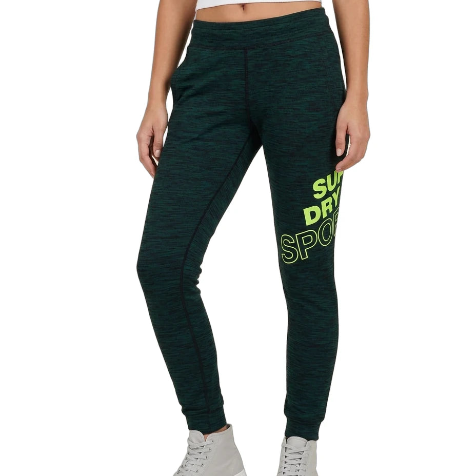A model wearing dark green heathered jogger sweatpants with a bright green graphic text print on the left leg, paired with a white crop top and light gray high-top sneakers, shown against a plain white background.