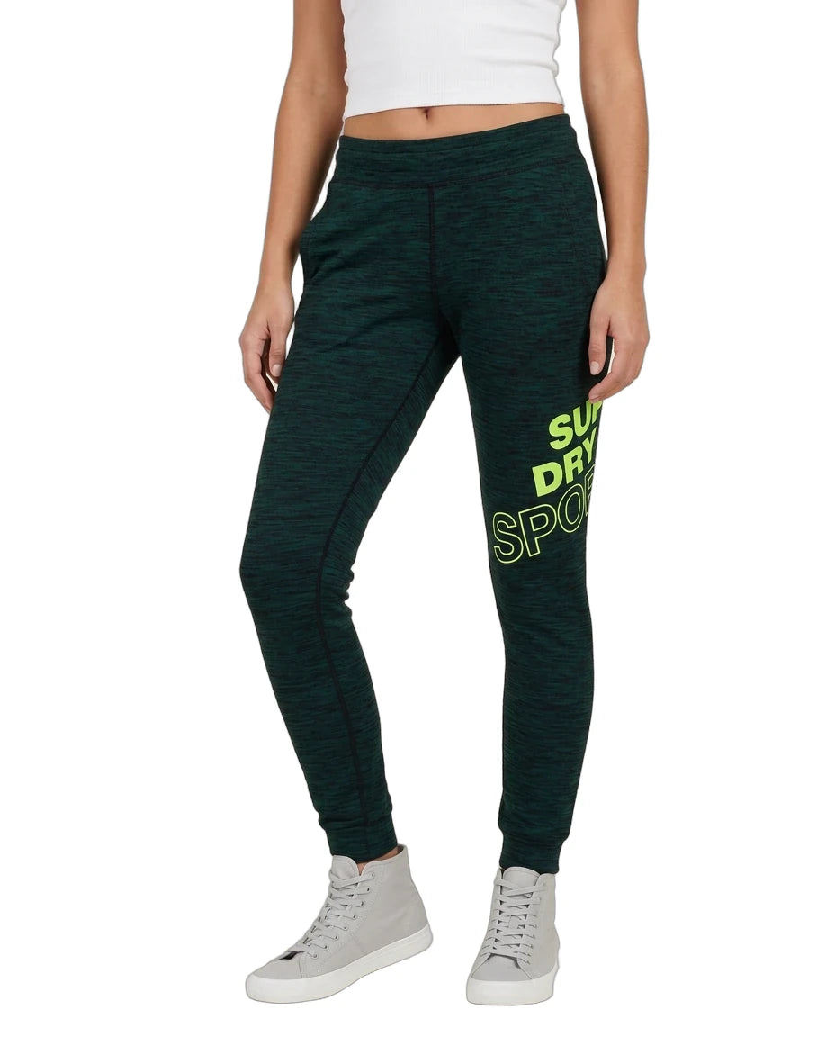 A model wearing dark green heathered jogger sweatpants with a bright green graphic text print on the left leg, paired with a white crop top and light gray high-top sneakers, shown against a plain white background.