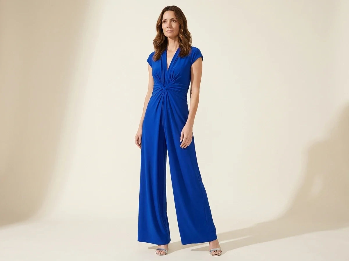 Brunette woman modeling a Vince Camuto royal blue cap-sleeve wide-leg jumpsuit with a twisted knot waist and nude heels.