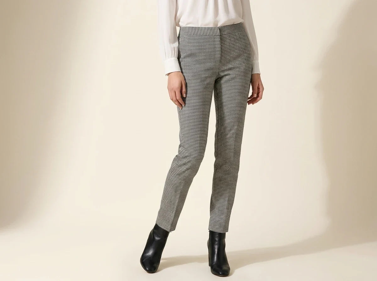 Cropped view of a woman wearing Vince Camuto black and white houndstooth skinny ankle pants, an ivory blouse, and black heeled boots.