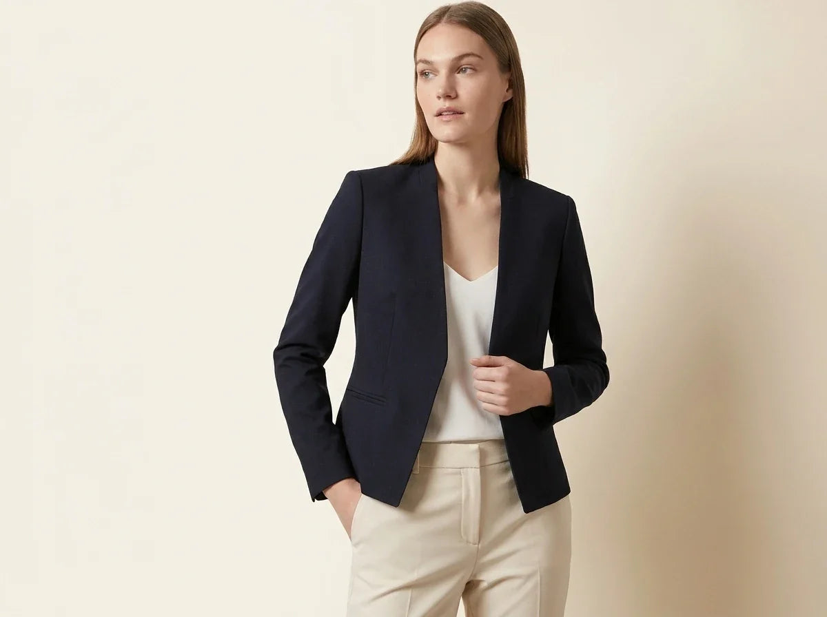 Blonde woman modeling a Calvin Klein navy blue collarless open-front tailored blazer over a white top and cream dress pants.