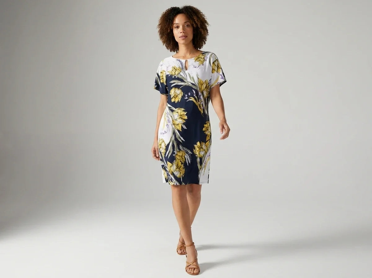 A woman modeling a short-sleeve knee-length dress with a navy blue, white, and yellow floral print, standing against a light gray studio background.