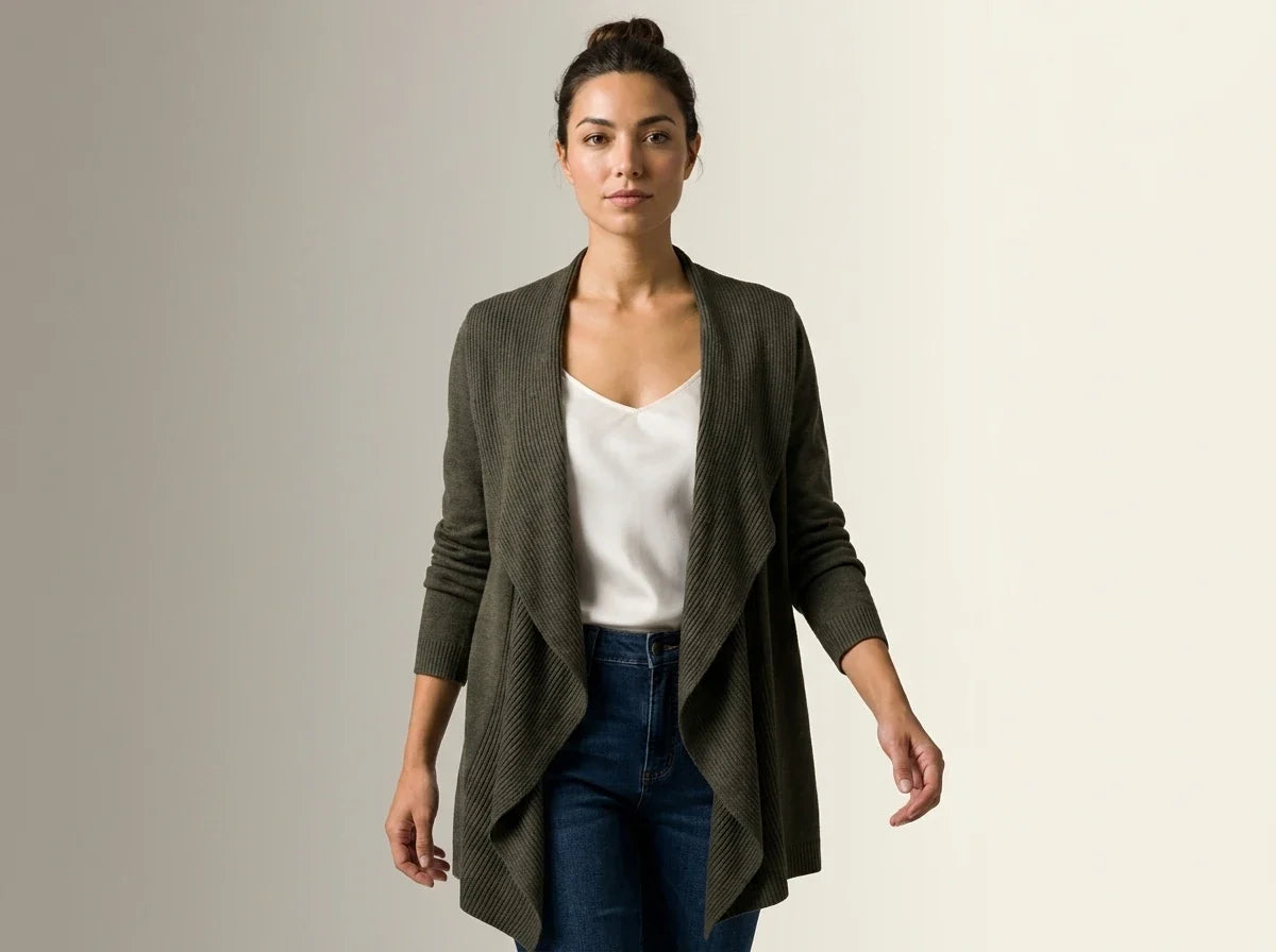 A woman modeling a dark olive green open-front knit cardigan over a white top and blue jeans, standing against a plain light gray studio background.