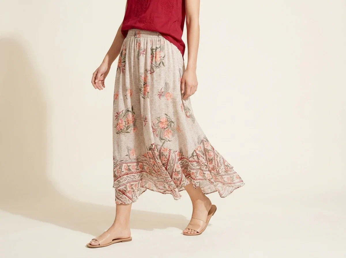 Cropped view of a woman wearing a flowy cream floral print maxi skirt with an elastic waistband and ruffle hem paired with nude slide sandals[cite: 26].