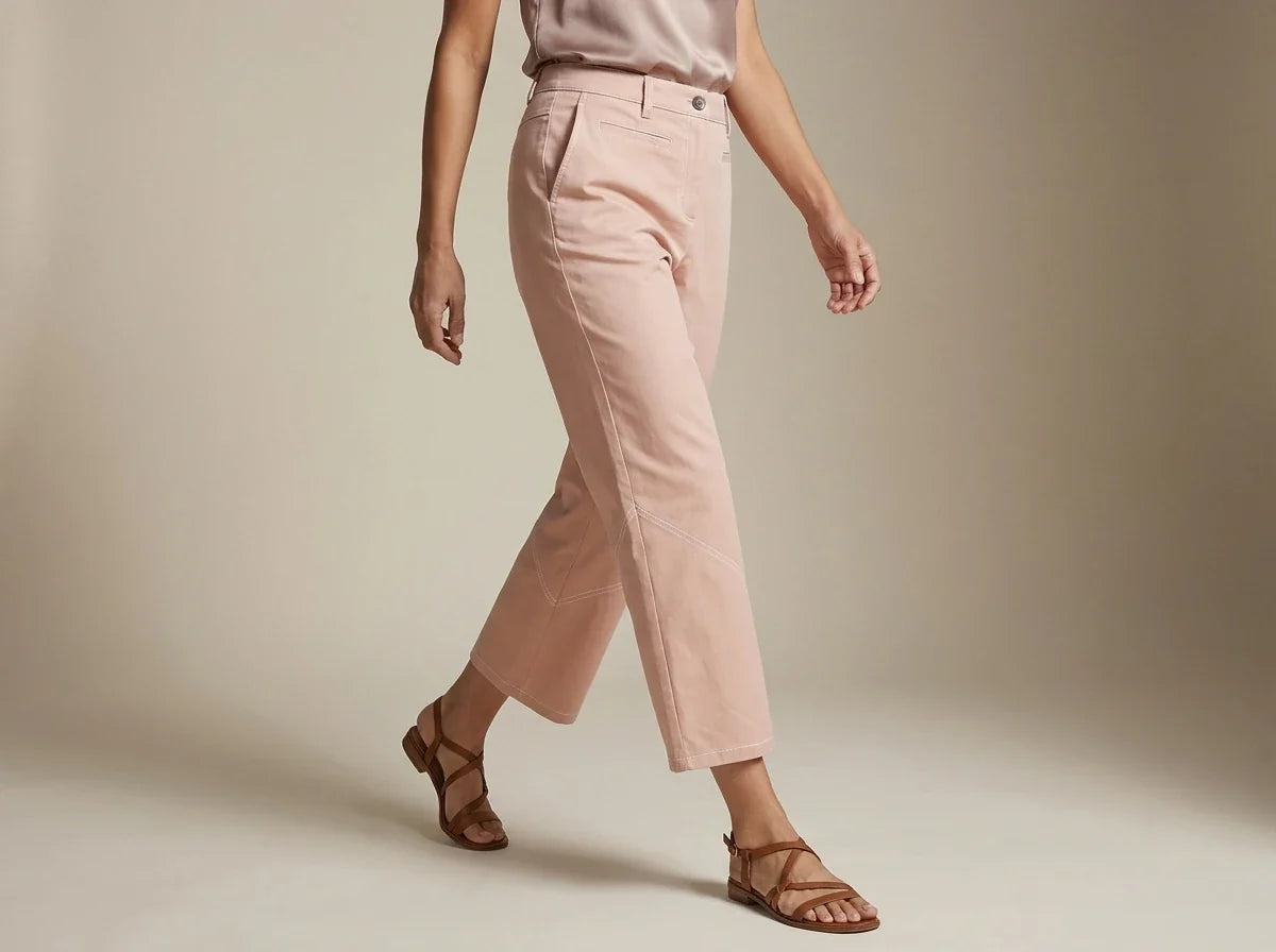 Cropped view of a woman wearing dusty pink straight-leg ankle pants and strappy brown flat sandals against a neutral studio backdrop.