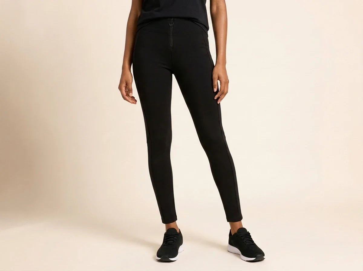 A model wearing black full-length leggings and black sneakers, shown from the waist down against a plain beige studio background.