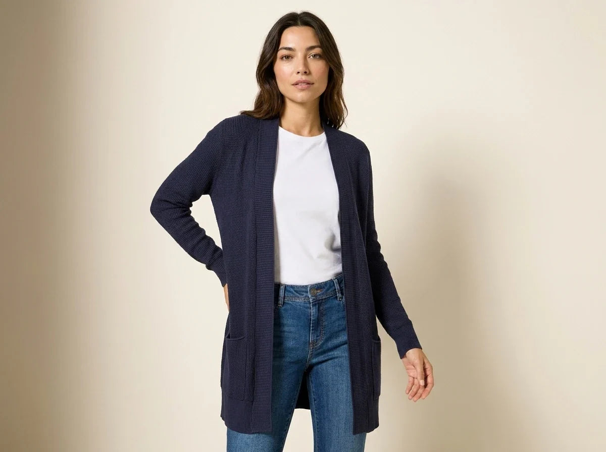 Brunette woman modeling an open-front navy blue waffle-knit cardigan sweater with patch pockets over a white t-shirt and blue jeans.