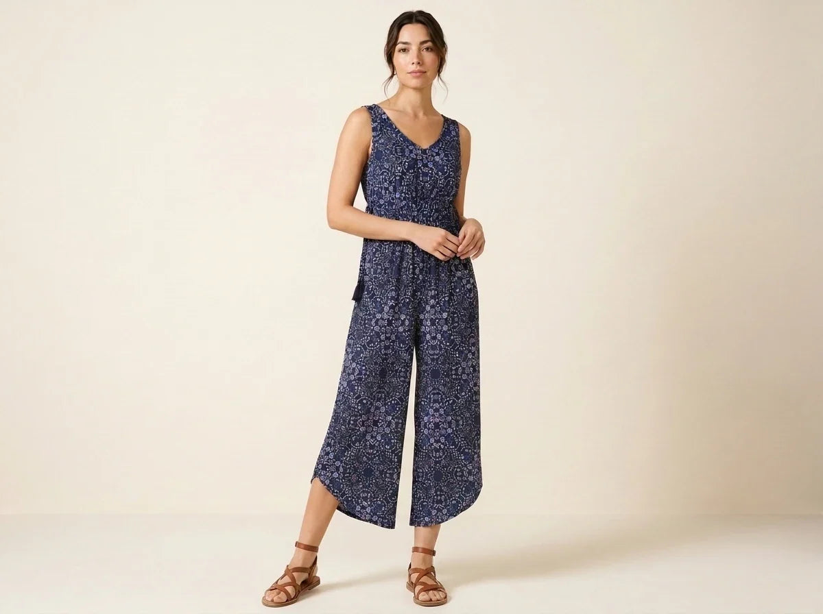 Brunette woman modeling a sleeveless navy blue floral print wide-leg cropped jumpsuit paired with brown strappy gladiator flat sandals.