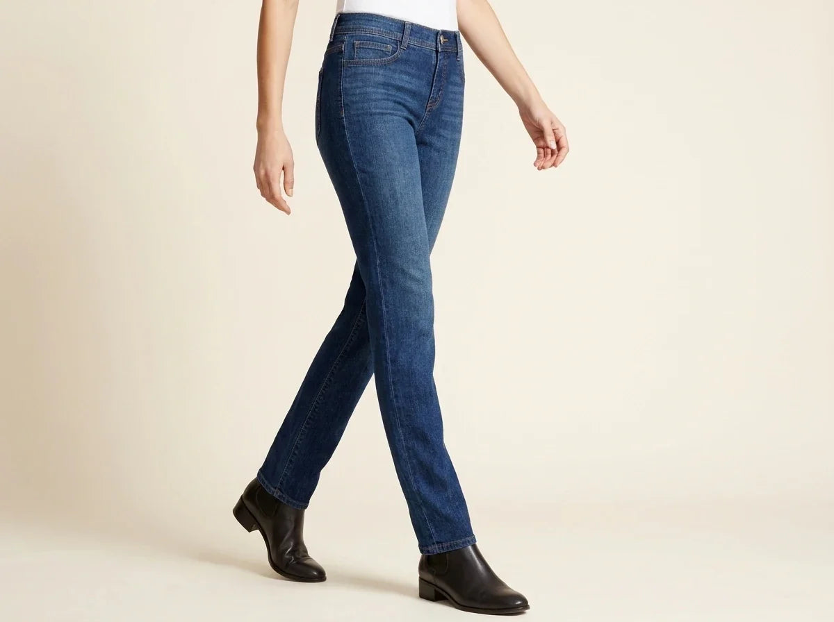 Cropped view of a woman walking in medium-wash straight-leg denim jeans paired with black leather Chelsea ankle boots and a white top.