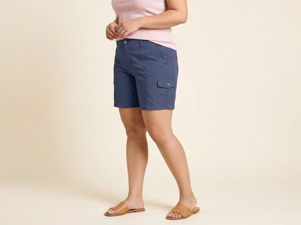 Cropped view of a woman wearing plus-size slate blue cargo utility shorts with flat tan leather slide sandals and a light pink top.