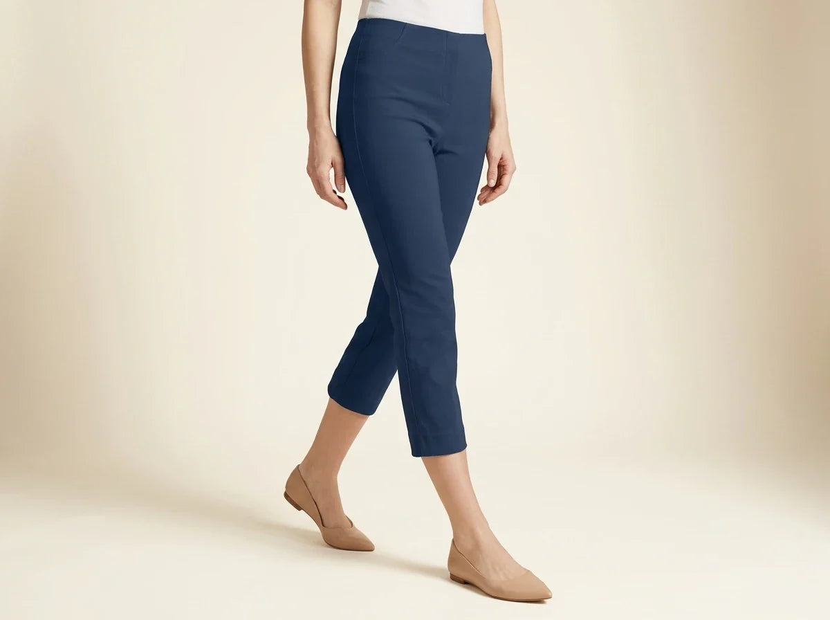 Cropped view of a woman wearing petite navy blue slim-fit cropped ankle pants paired with nude pointed-toe flat shoes.