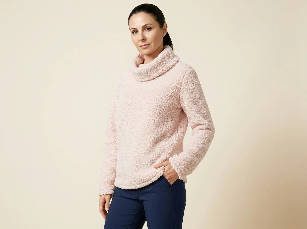Brunette woman modeling a petite blush pink fuzzy sherpa fleece cowl-neck sweater paired with navy blue pants.