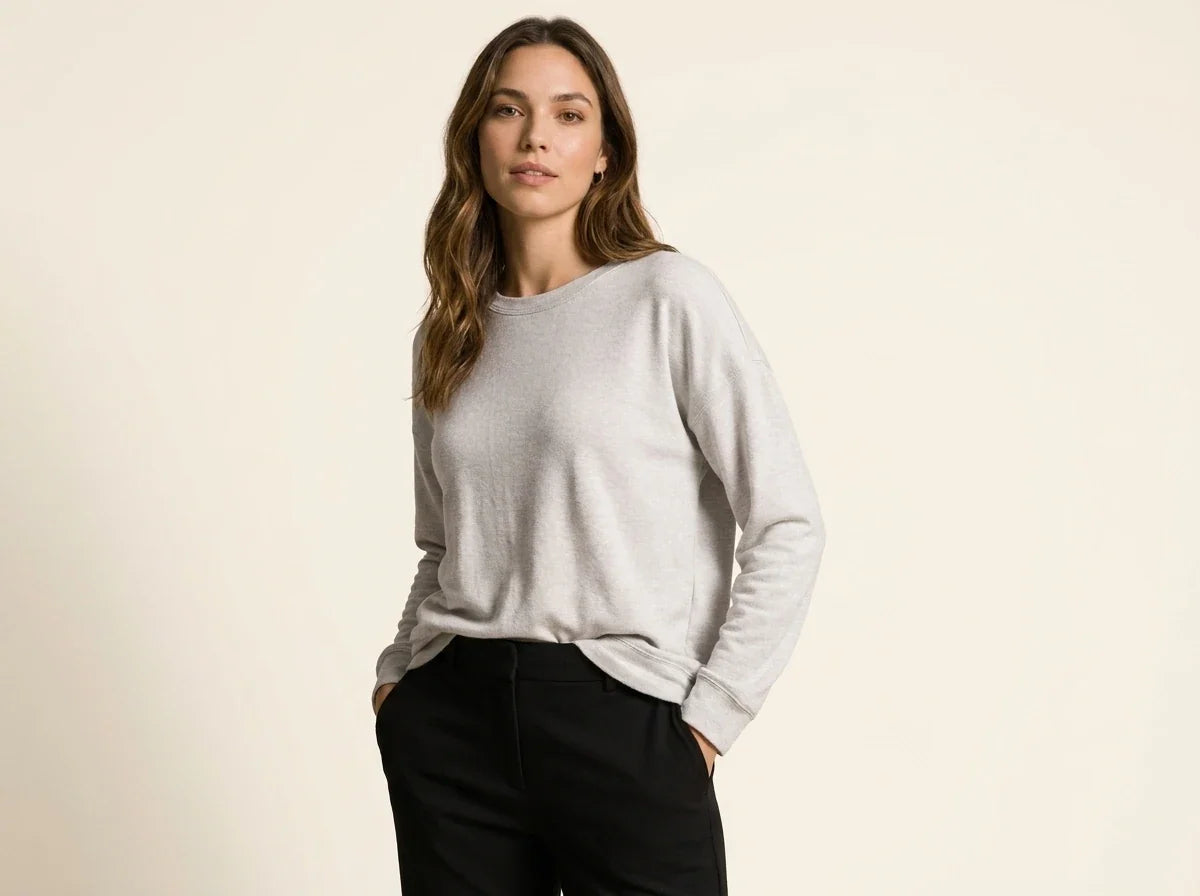 Brunette woman modeling a light heather grey crewneck pullover sweater paired with black trousers.