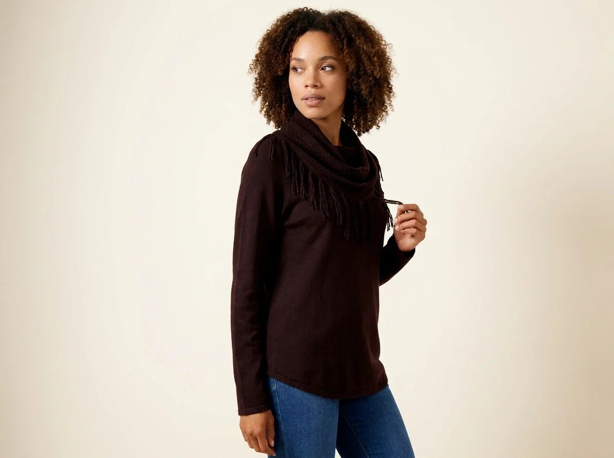 Woman with curly brown hair modeling a dark chocolate brown cowl-neck sweater with fringe trim paired with blue jeans.