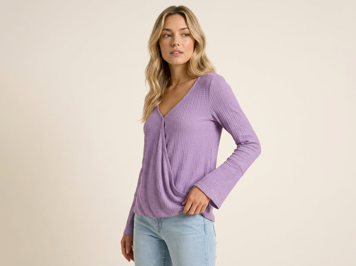 Blonde woman modeling a lavender purple waffle-knit crossover top with bell sleeves and light wash jeans.
