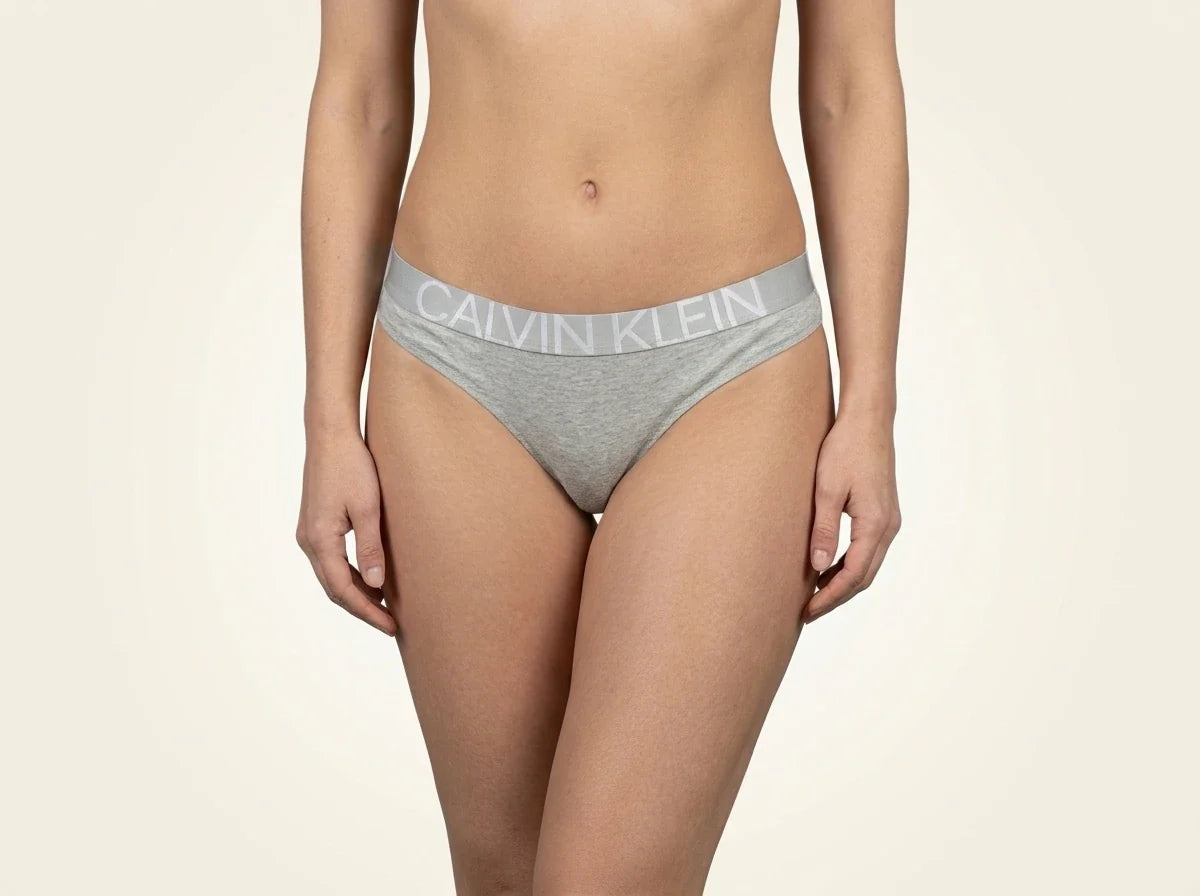 Cropped view of a woman wearing heather grey Calvin Klein cotton thong underwear with a signature logo elastic waistband.