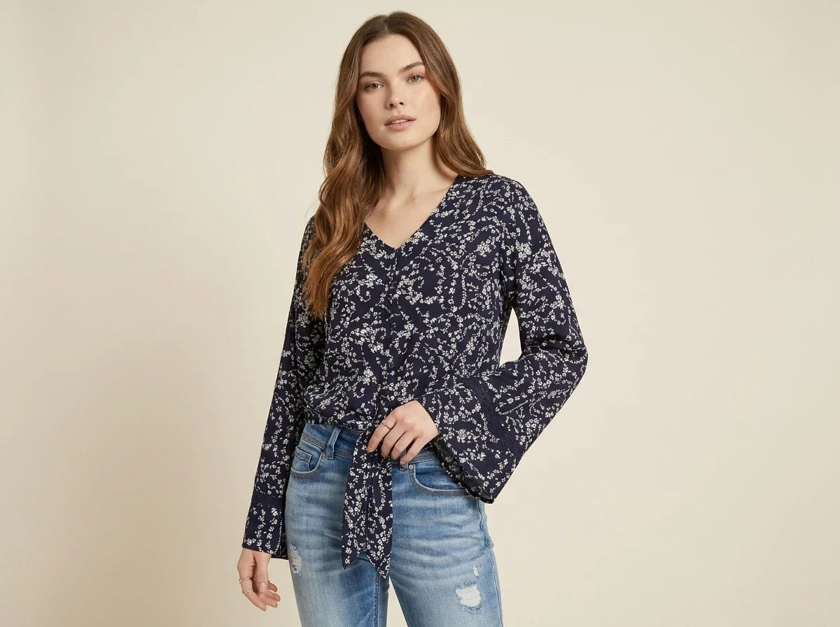 Brunette young woman modeling a navy blue floral tie-front blouse with flared bell sleeves and distressed denim jeans.